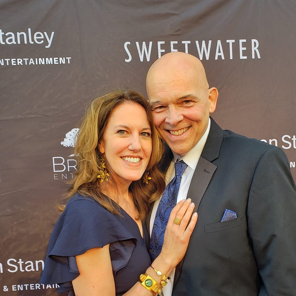 Smiling couple dressed formally, posing together at a red carpet event in front of a backdrop with the logos “Sweetwater” and “Morgan Stanley.”