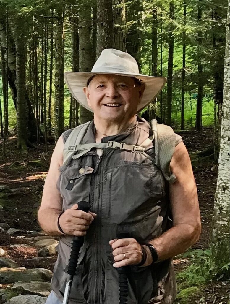 and elderly man with a tan bucket hat on with outdoor gear on standing on the Appalachian trail hiking. 
