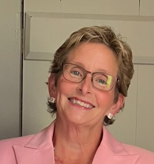 Short blond haired woman with glassed wearing a pink suit and smiling large